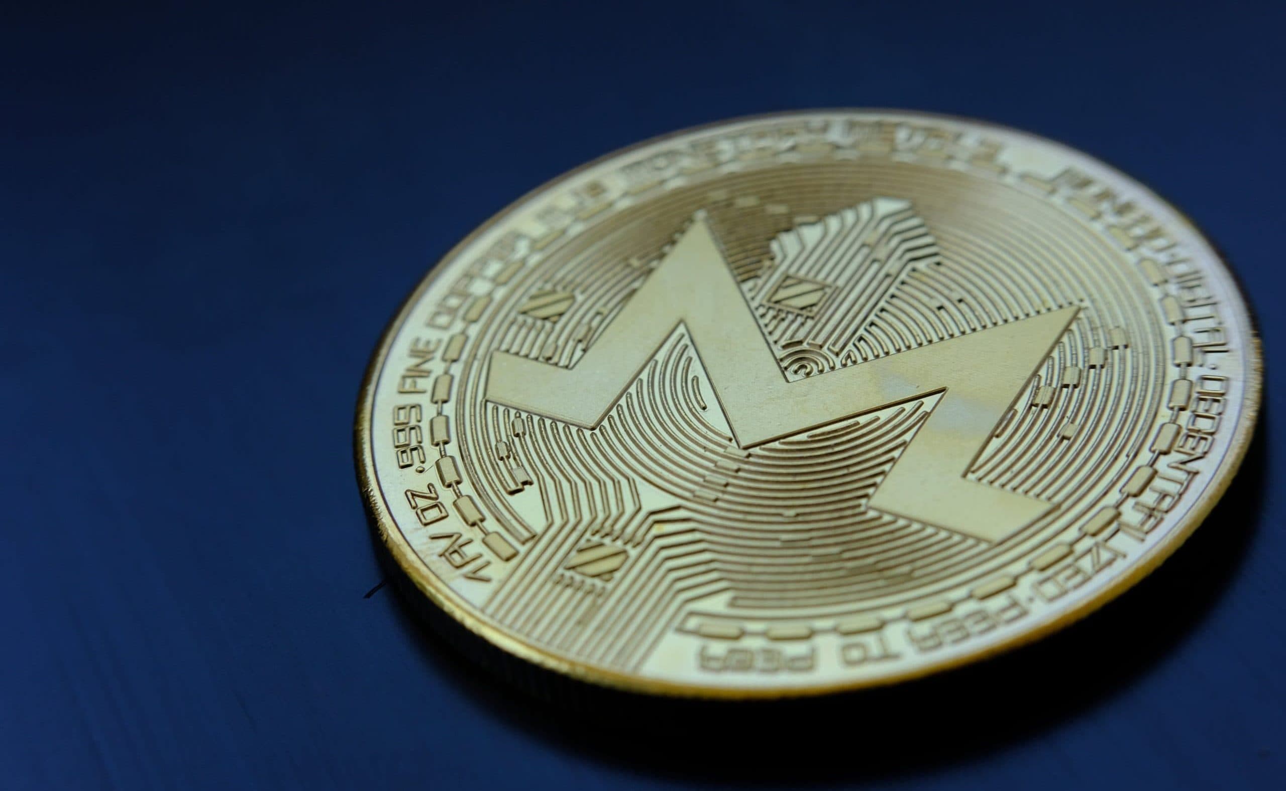 Eine goldene Monero-Kryptowährungsmünze mit dem Monero-Logo liegt auf einer dunkelblauen Oberfläche.